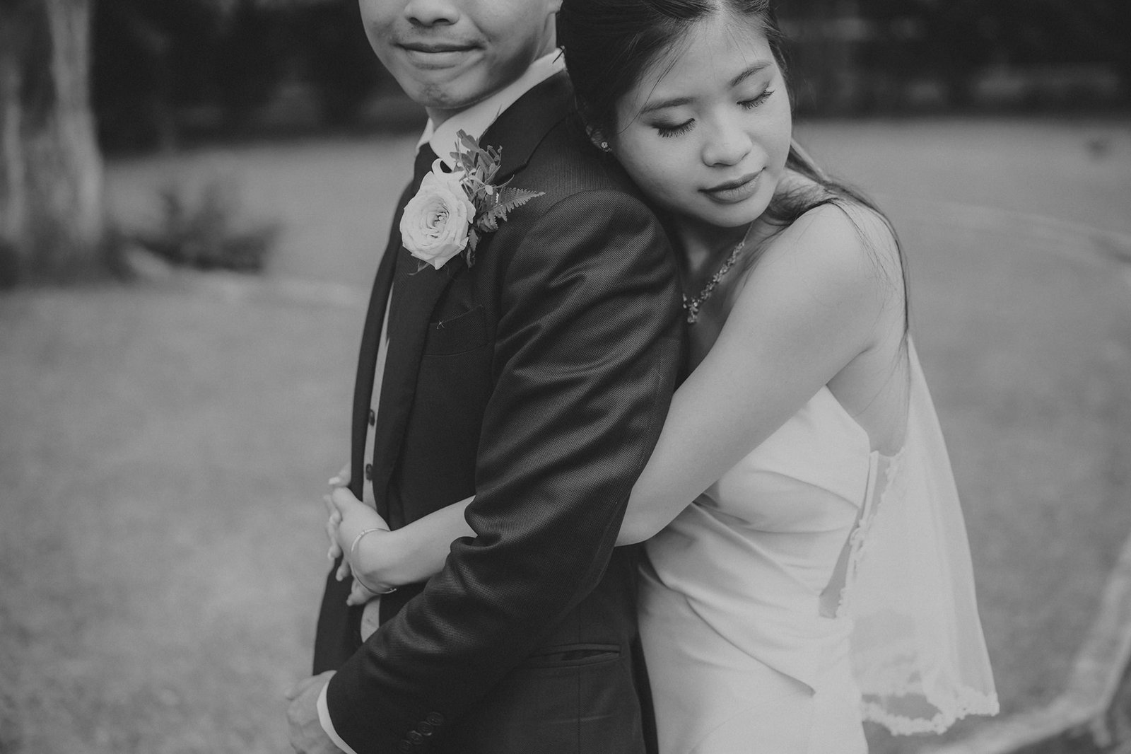 A bride in a flowing gown embraces her groom, who wears a suit and boutonniere, in a tender wedding portrait.