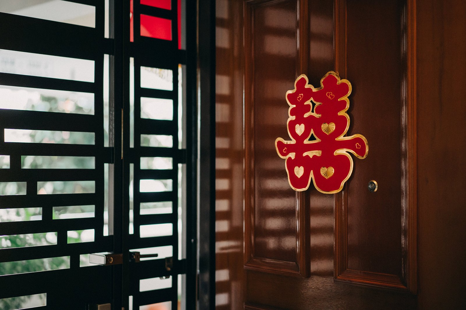 A vibrant red Chinese double happiness symbol adorns a polished wooden door, with a black geometric gate visible to the left.