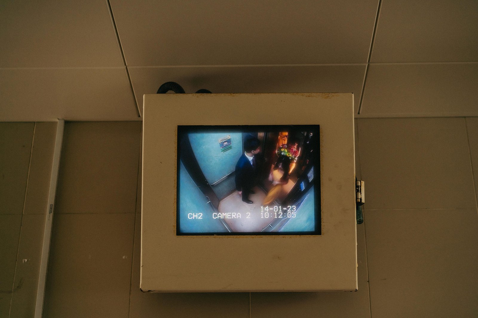 A security camera feed shows a man in a suit entering an elevator with a date and time stamp: 14-01-23 10:12:05.