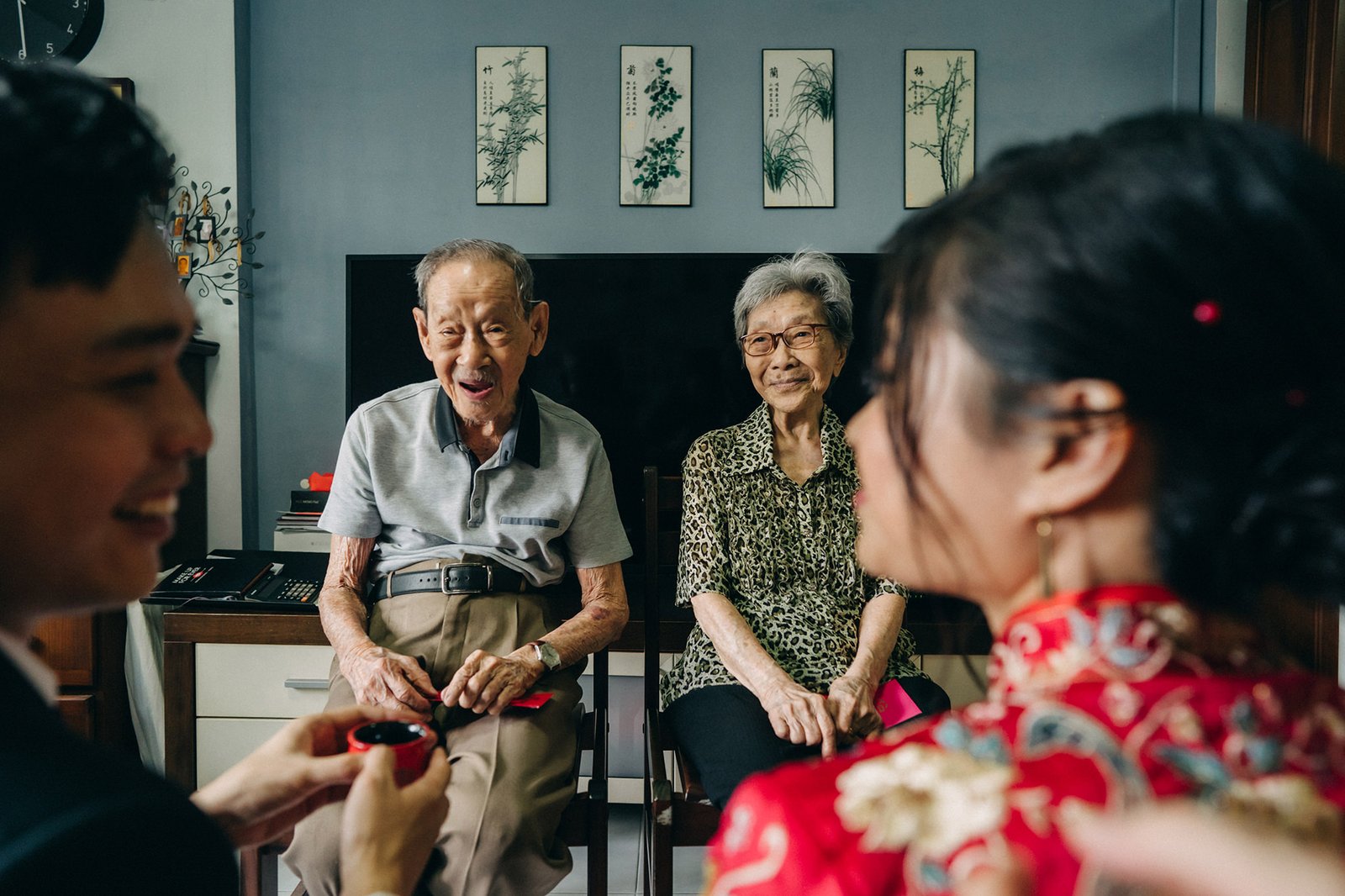 A joyful elderly Asian couple beams as a young couple in traditional Chinese attire offers them tea during a wedding ceremony, symbolizing respect and family bonds.