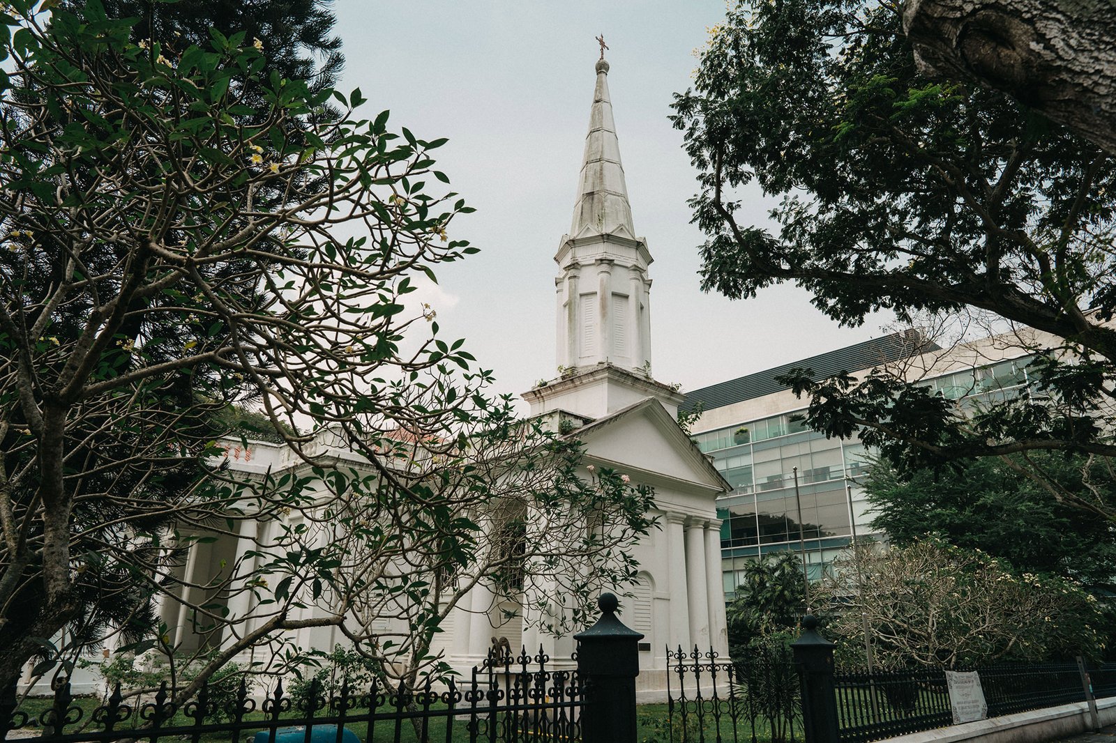 White church steeple with trees and modern building at Armenian Church Singapore