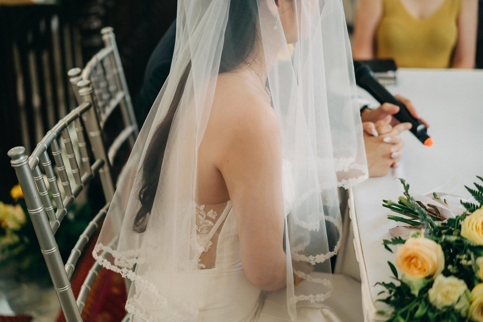 Bride in a white veil with lace details sitting at a table with flowers