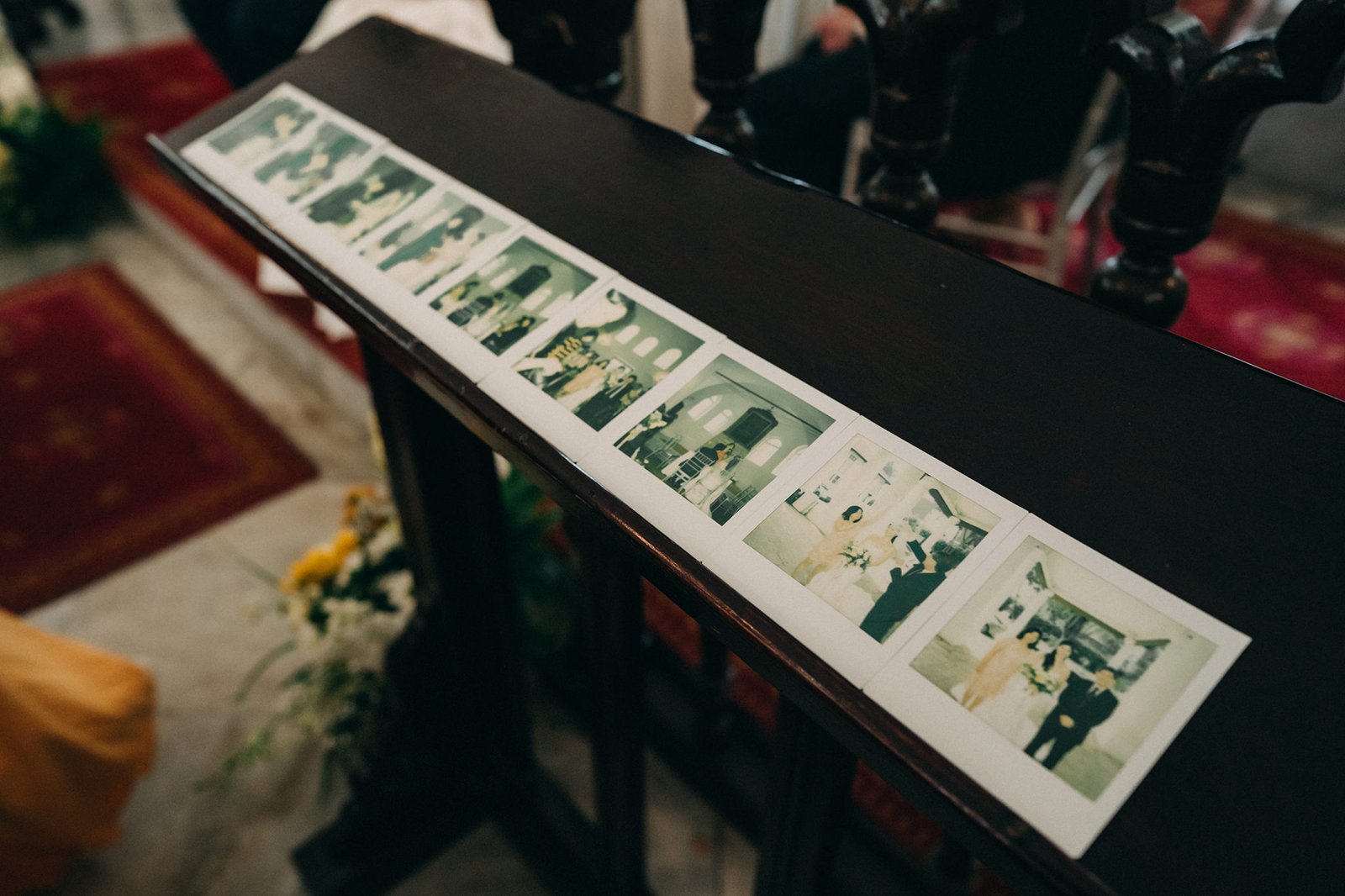 A strip of wedding photos, featuring a bride and groom in various poses, is displayed on a dark wooden surface, possibly a church pew, with red carpet and floral arrangements in the background.