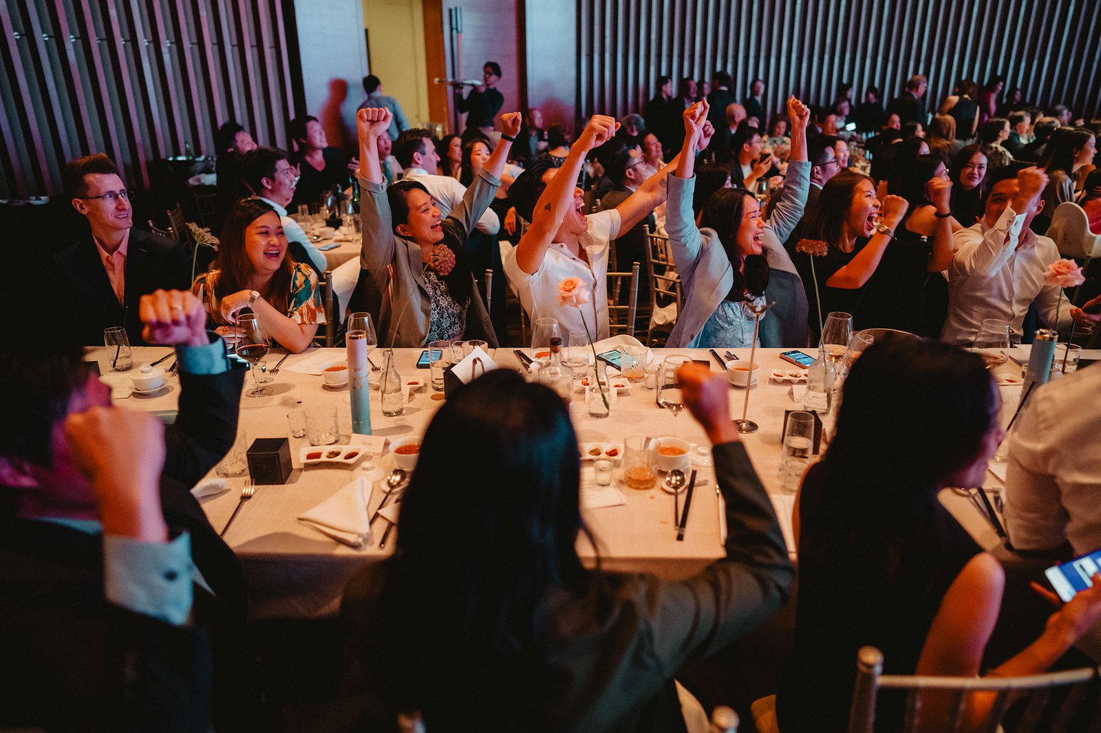 Guests celebrating at a Capella Singapore wedding reception, raising fists in excitement.