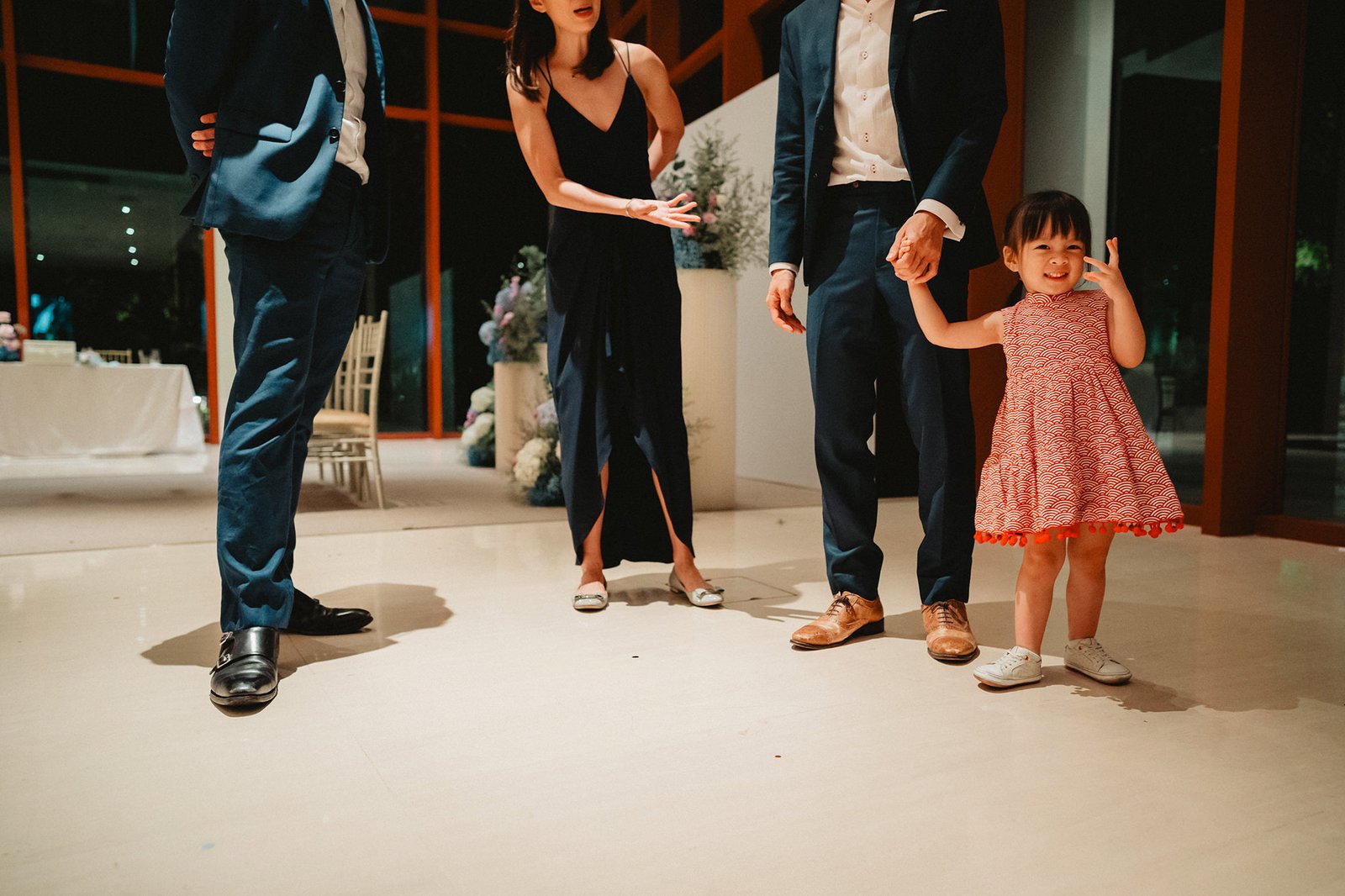 A young girl in a red dress holds hands with an adult at a Capella Singapore wedding.