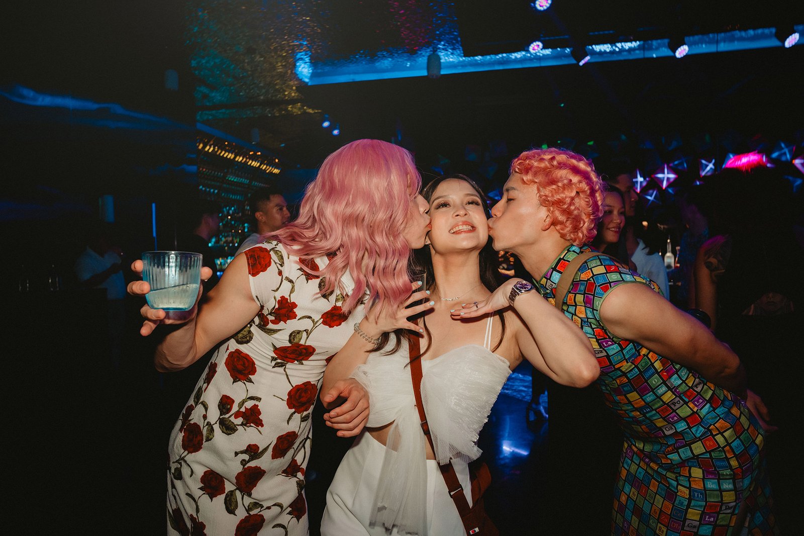 Capella Singapore wedding: Two people in colorful wigs kiss a woman in white.