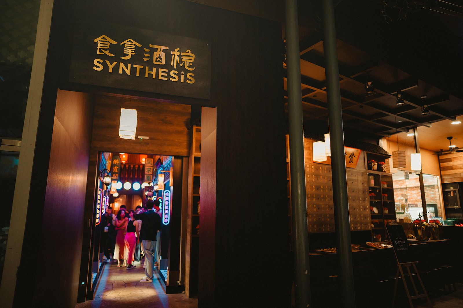 Restaurant entrance with "SYNTHESIS" sign, illuminated by lanterns.
