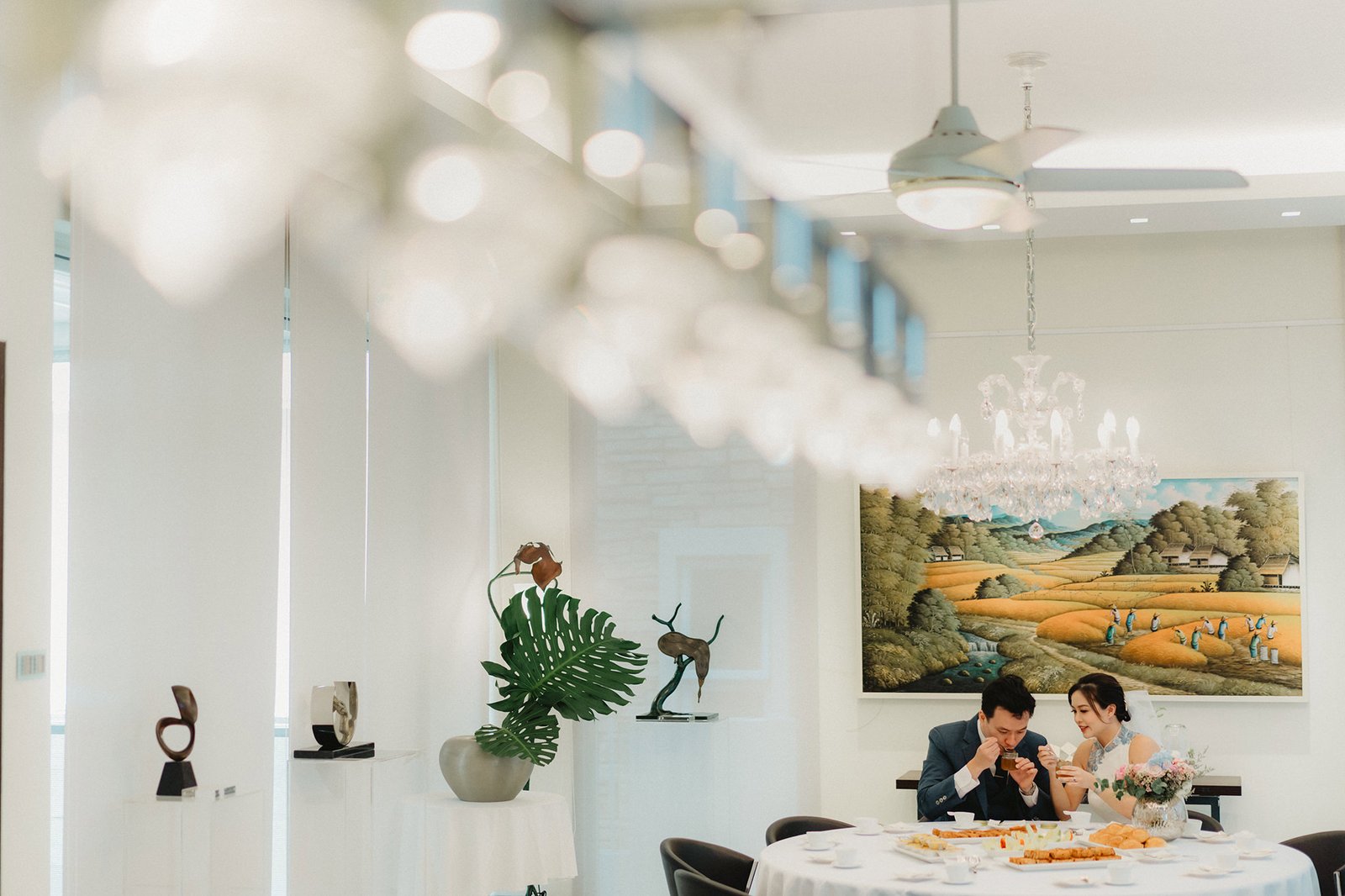 Han & Ming enjoy a meal at their Capella Singapore wedding, with a painting in the background.