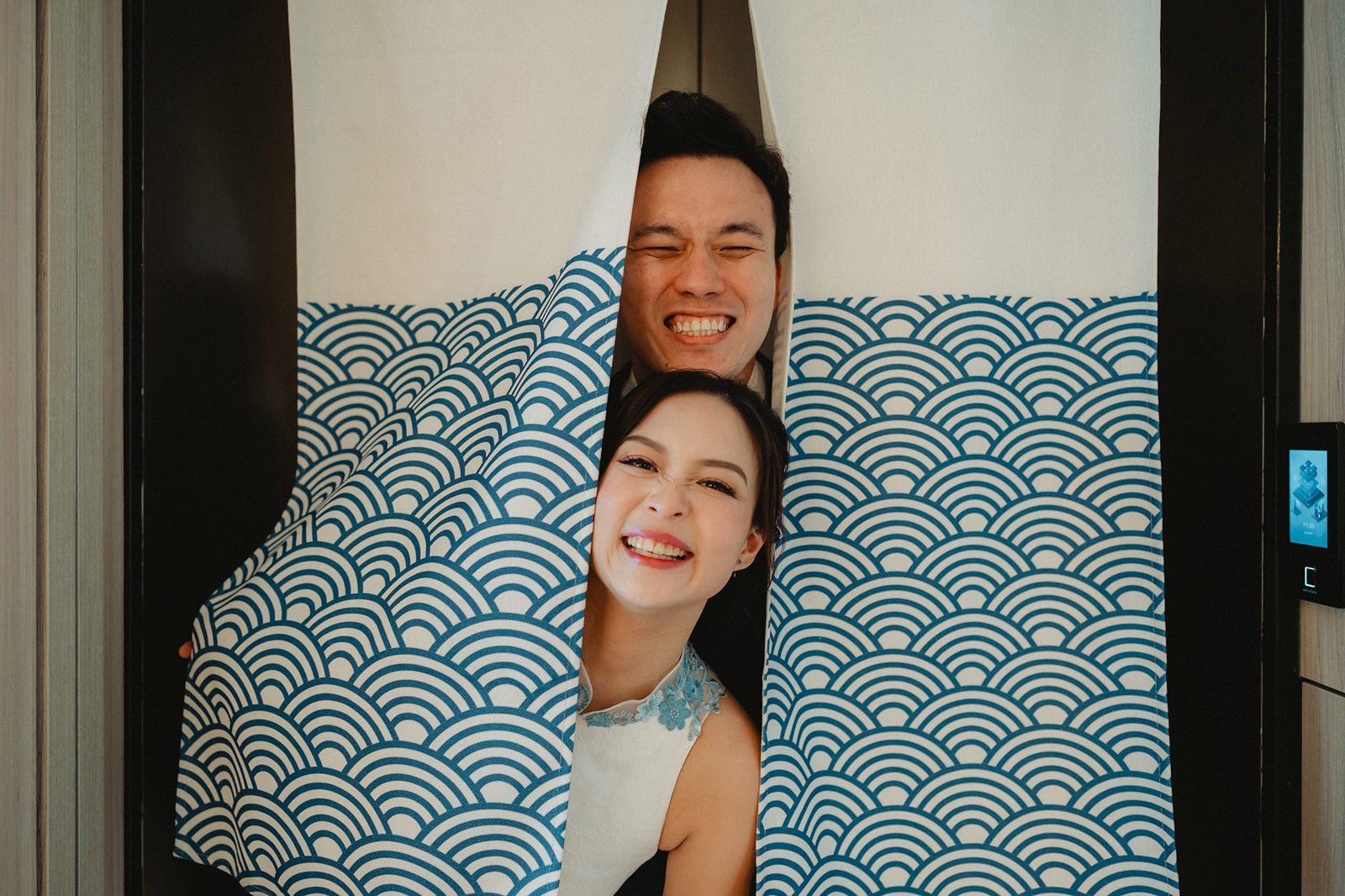 Han and Ming share a joyful moment at their Capella Singapore wedding, peeking through blue wave curtains.