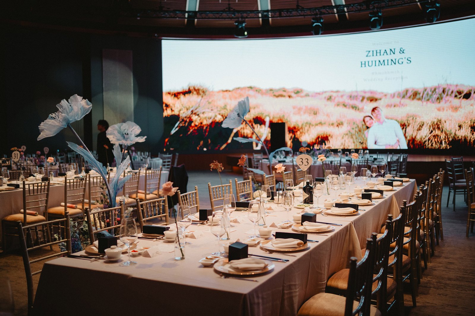 Capella Singapore wedding reception setup with elegant table settings and a large screen displaying a couple.